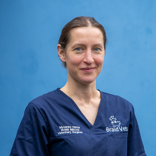 Person in a blue veterinary uniform with embroidered text Braid Vets stands against a plain blue background, looking at the camera.
