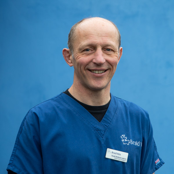 Smiling person in a blue uniform with a name badge, standing against a blue background.
